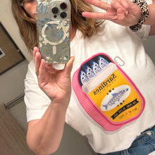 Person holding a phone wearing a white tee shirt with a sardine can design.