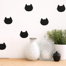 Black cat face decals on a white wall with decorative vases and plants below.