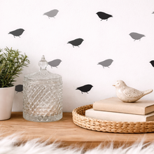 Decorative shelf with a plant, glass jar, books, and bird figurine against a wall with bird decals.