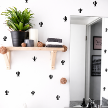 Bathroom with cactus wall decals, a shelf with plants and towels, and a mirror.