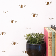 Potted plant on a wooden surface with decorative wall stickers of eyes and winking faces.