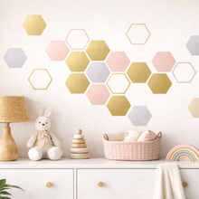 Hexagonal wall decor in pastel colors on a white wall above a shelf with toys and a lamp.