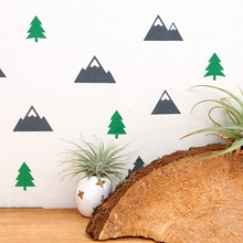 Decorative wall with mountain and tree decals, a wooden log, and air plants.