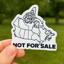 Sticker of a map outline with 'Not for Sale' text held by a hand against a blurred green outdoor background