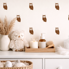 Decorative shelf with owls, candles, and other items against a wall with owl decals.
