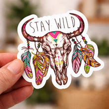 Sticker with a bull skull design and 'Stay Wild' text held by a hand.