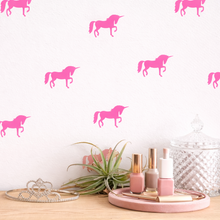 Pink unicorn decals on a white wall with decorative items on a wooden surface.